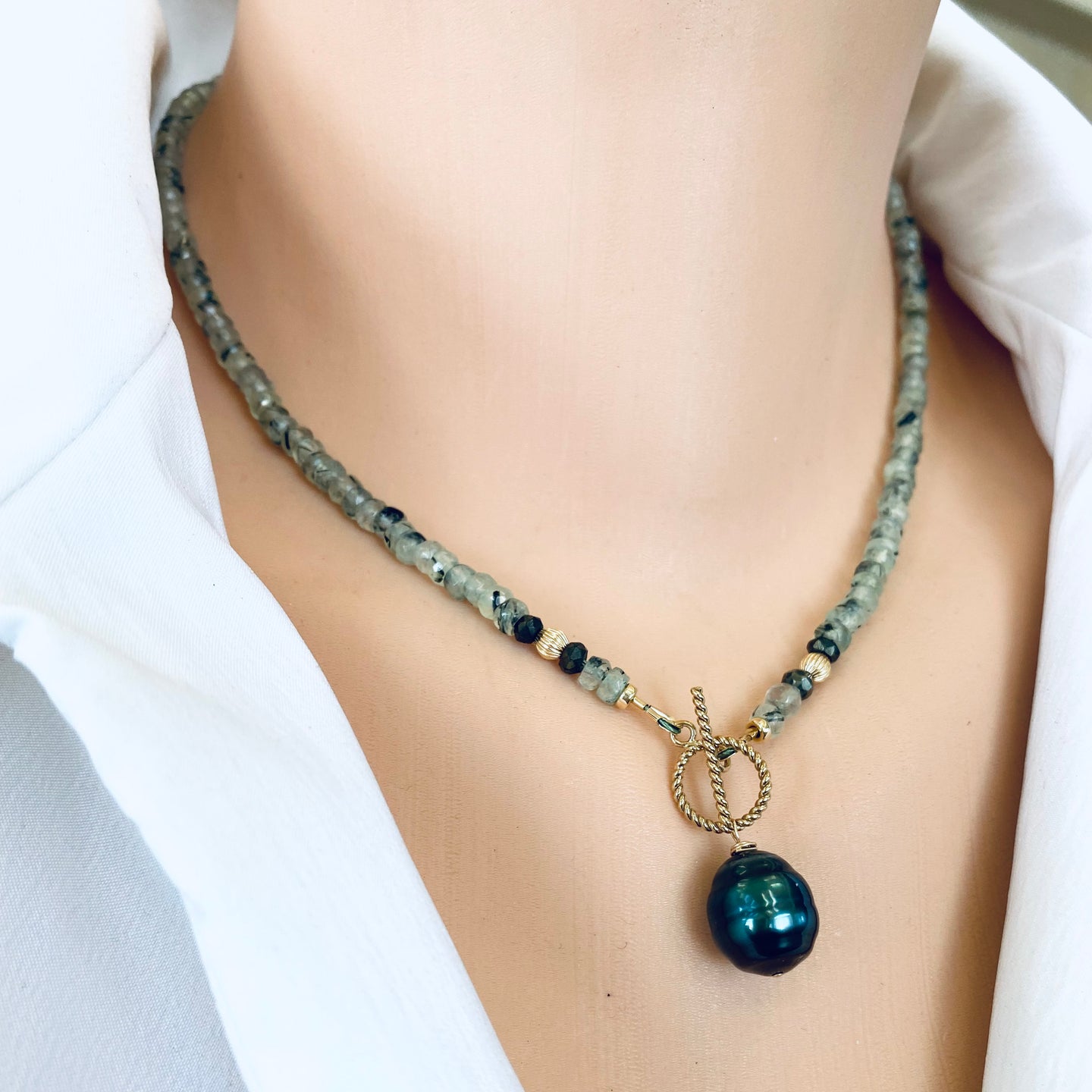 This necklace features a delicate chain of soft, translucent faceted green Prehnite rondelle beads, beautifully complemented by a striking Tahitian baroque pearl as the centerpiece pending from a cold filled toggle clasp. 18